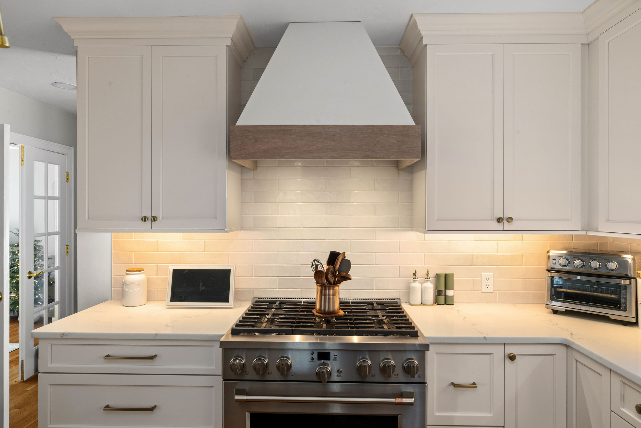 White range hood with wood trim over a gas range and subway tile in a Hanover kitchen