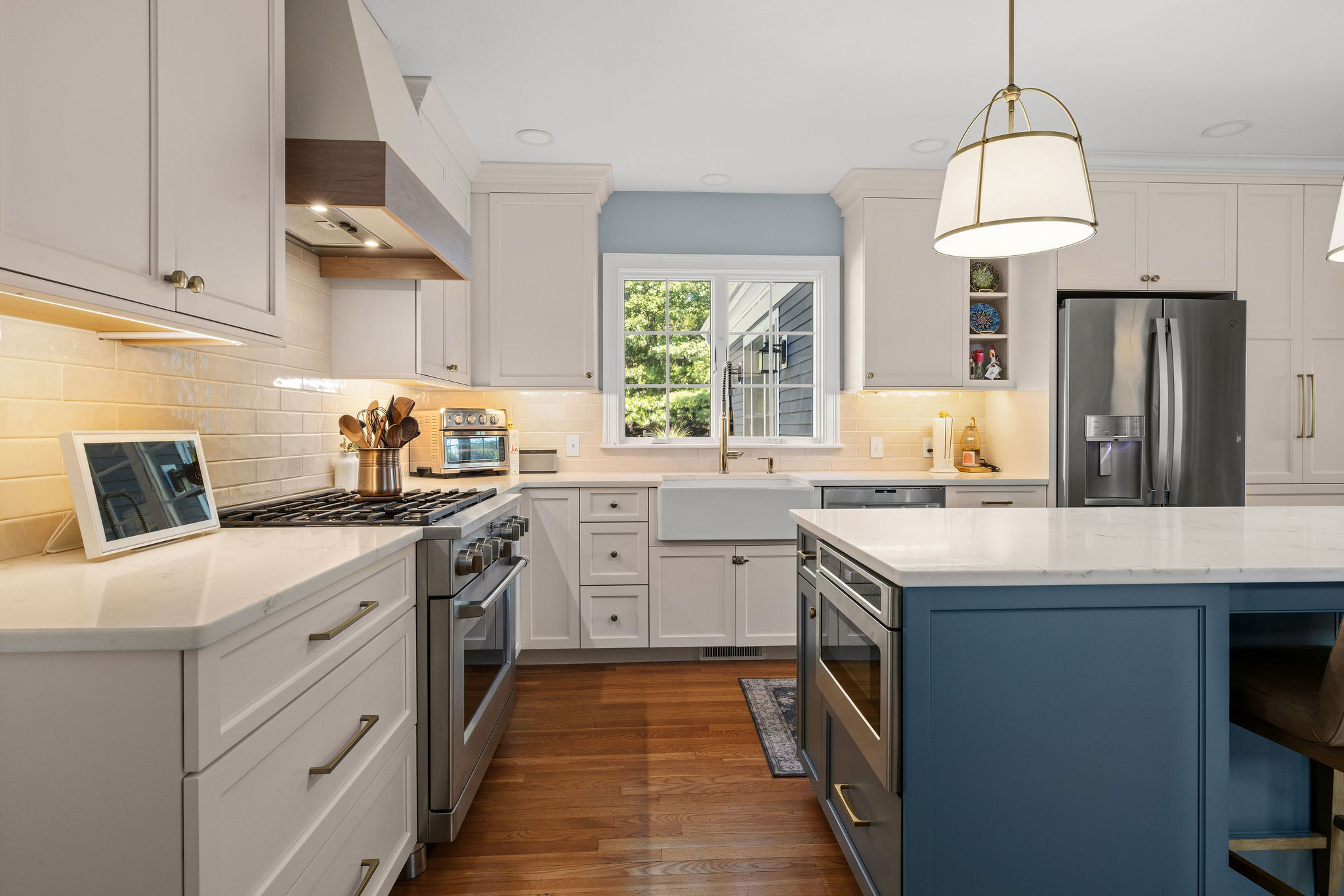 White cabinetry and a Seaglass island with a farmhouse sink and gas range in a Hanover kitchen