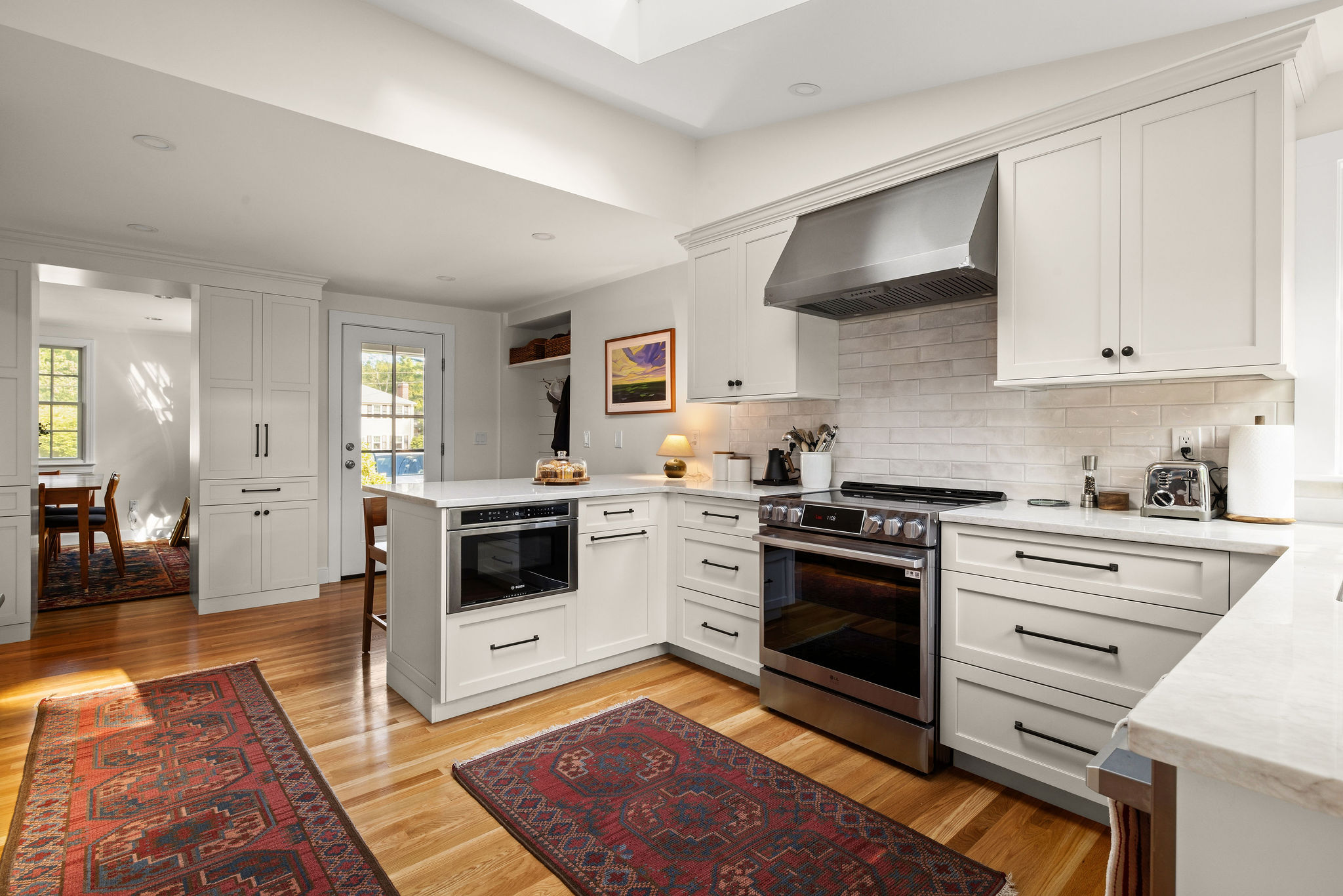 White Hingham kitchen open to the dining room with a built-in microwave, pantry cabinets, and wood floors