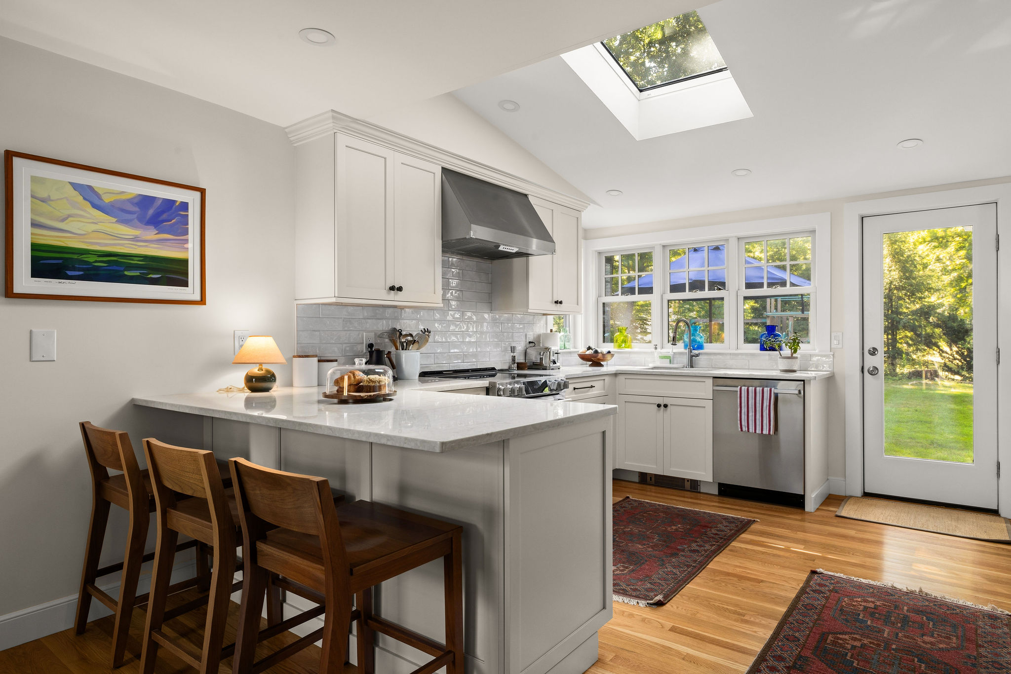 White Hingham kitchen with a peninsula, counter stools, skylight, and yard access