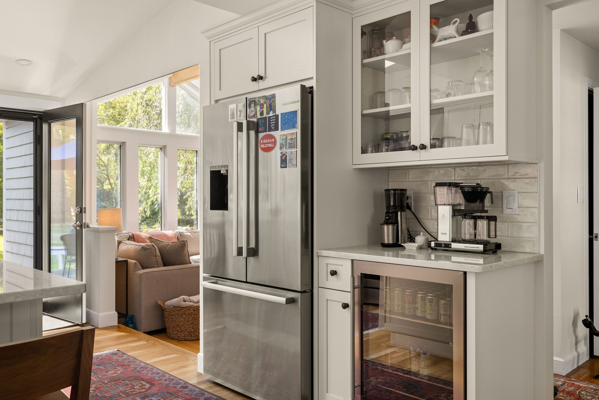 White kitchen with a beverage fridge, glass-front cabinets, and coffee station open to the living room in Hingham
