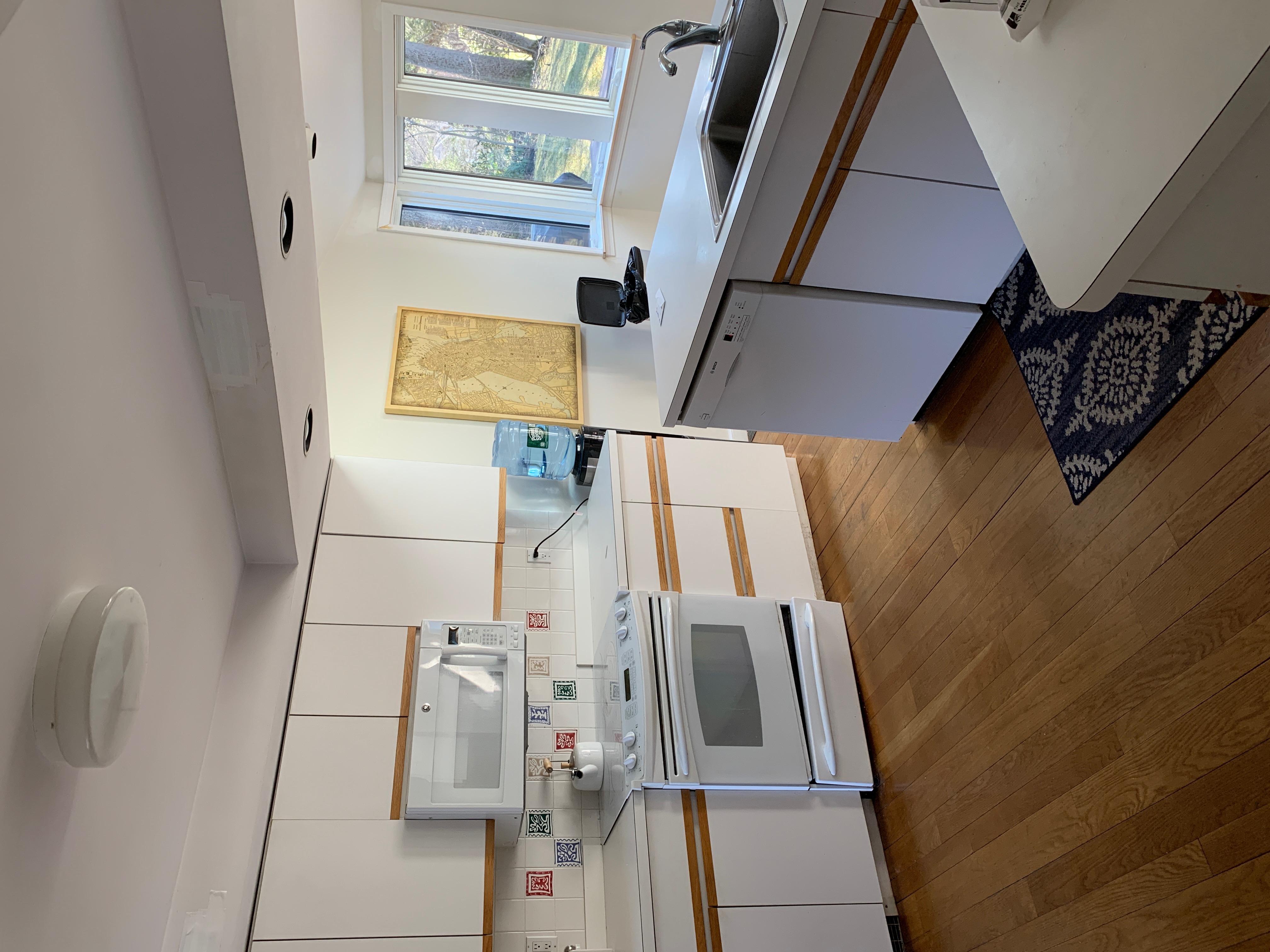 Before renovation: the original Hingham kitchen with white laminate cabinets, a wall microwave, and decorative tile backsplash