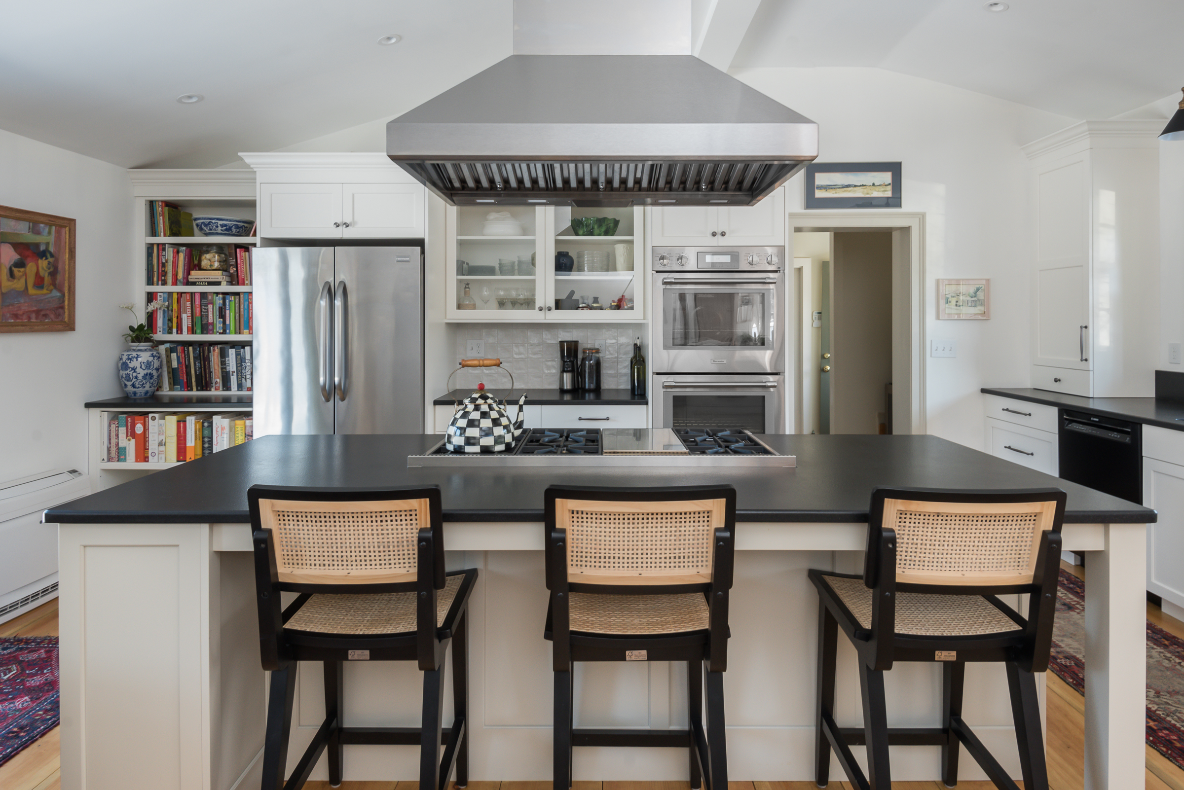 Kitchen island with black stone counter and cane counter stools in a Duxbury remodel