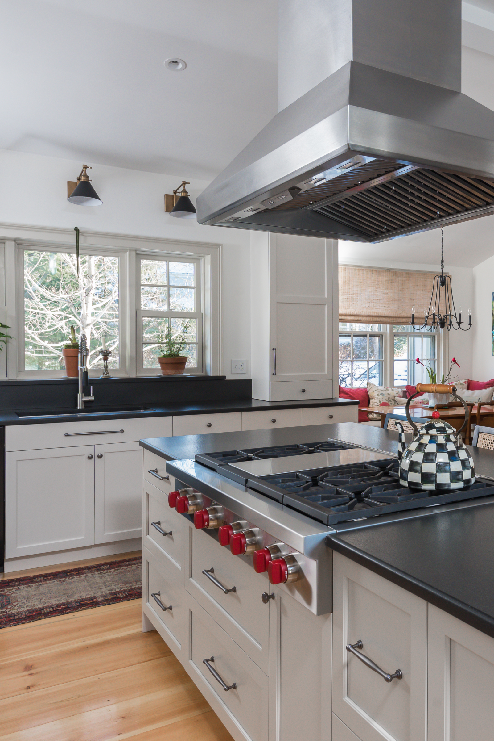Island range top with red knobs under a stainless hood, with the window wall behind