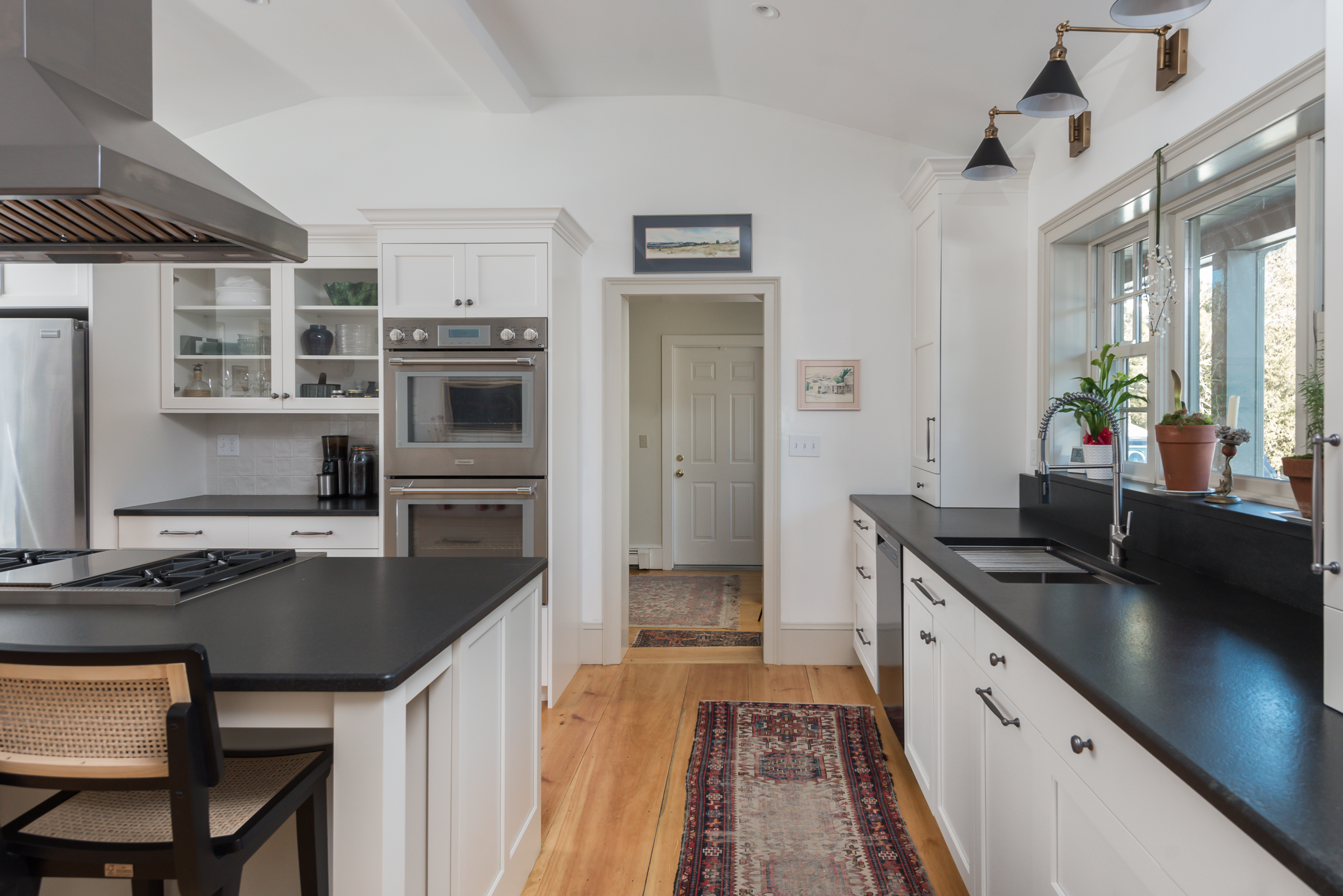 Sink wall with black stone counters and brass sconces, with a widened doorway to the hall