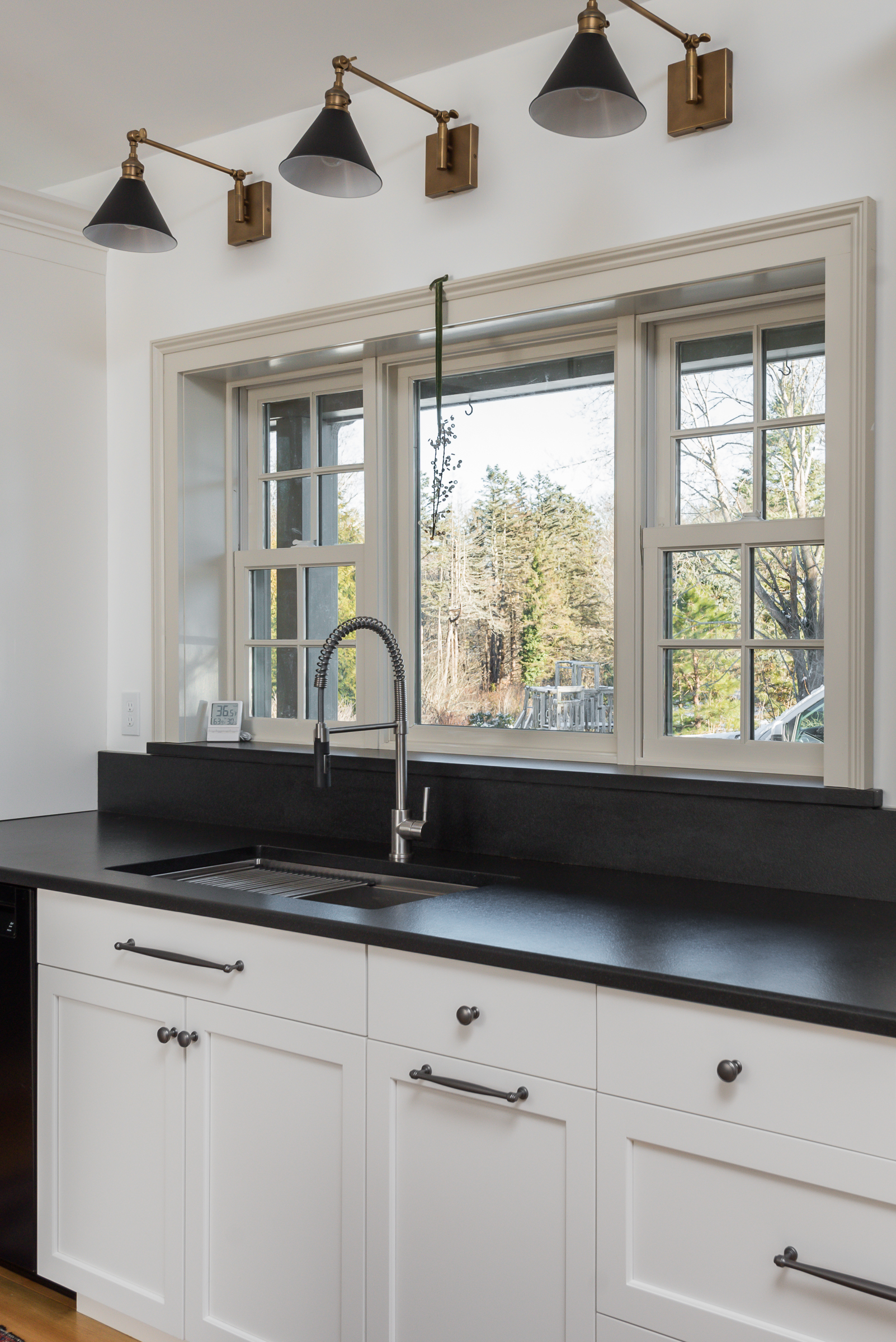 Undermount sink and pull-down faucet under a triple window with black and brass sconces