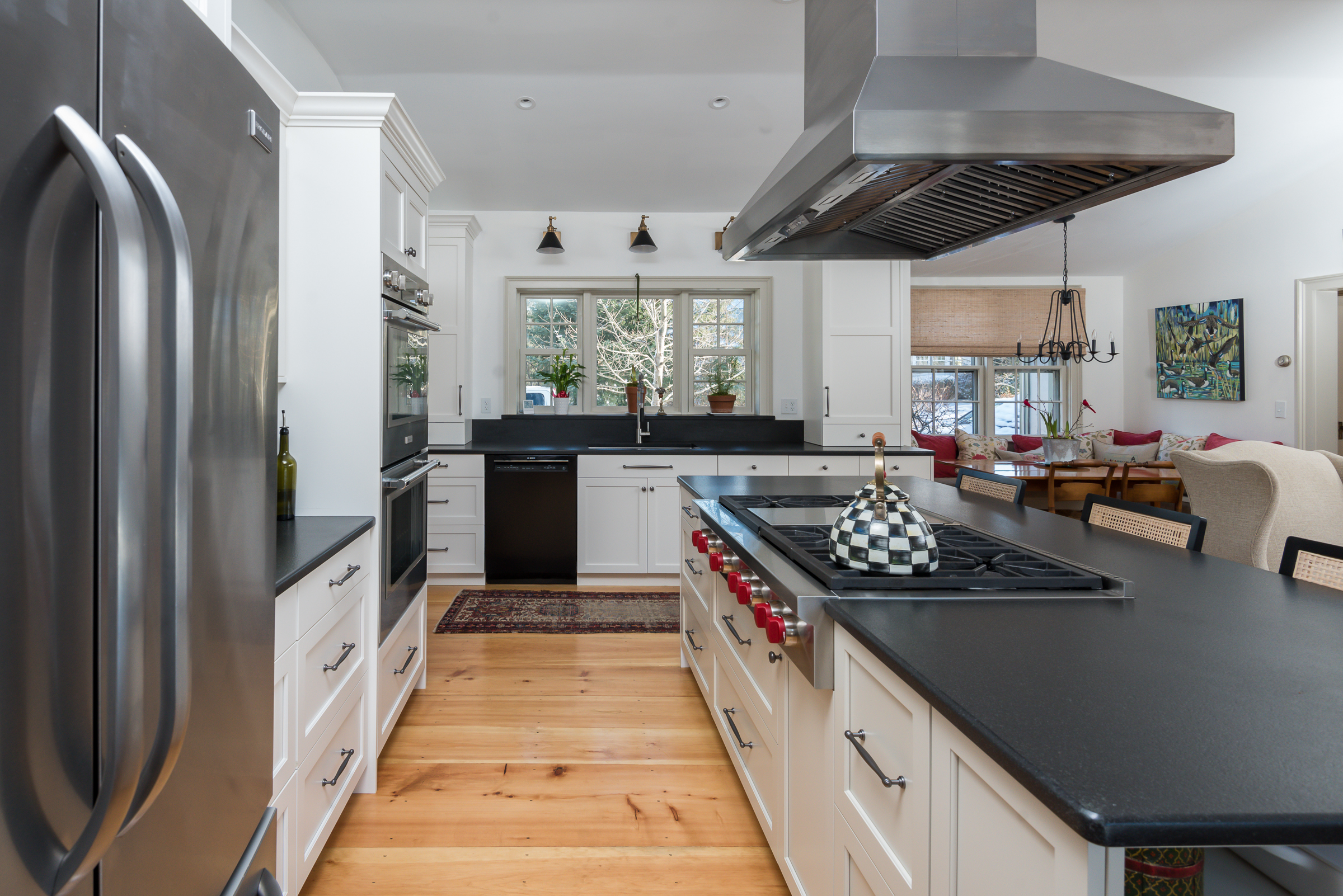 View down the island to the window wall, with wide pine floors and a stainless refrigerator