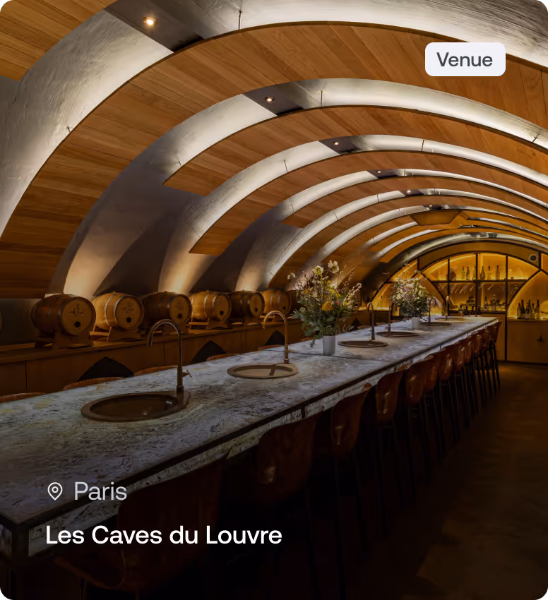 Interior of Les Caves du Louvre in Paris with arched wooden ceiling, long marble table, bar stools, and wine barrels.