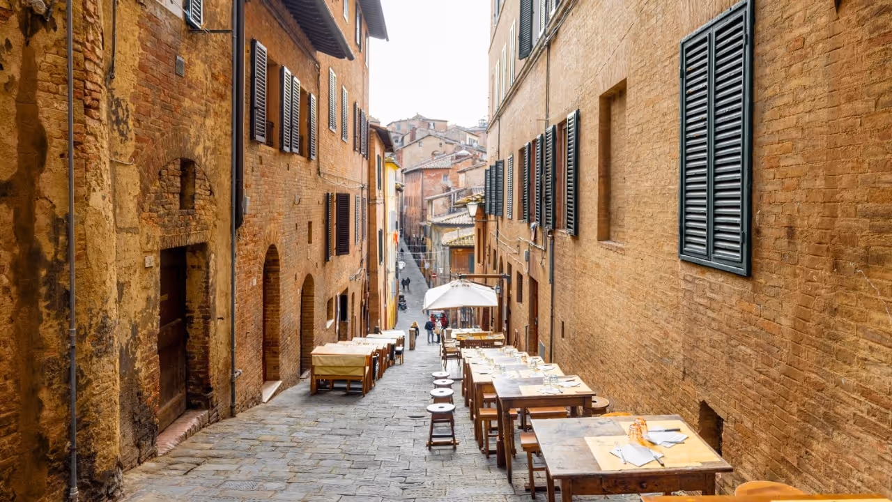 A narrow medieval street in Siena's historic centre — restaurants and gelato nearby.
