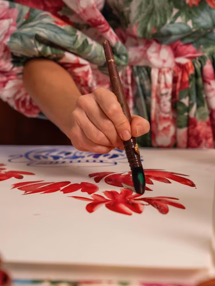 Serena painting red poppy petals with a fine brush, wearing a floral-print dress.