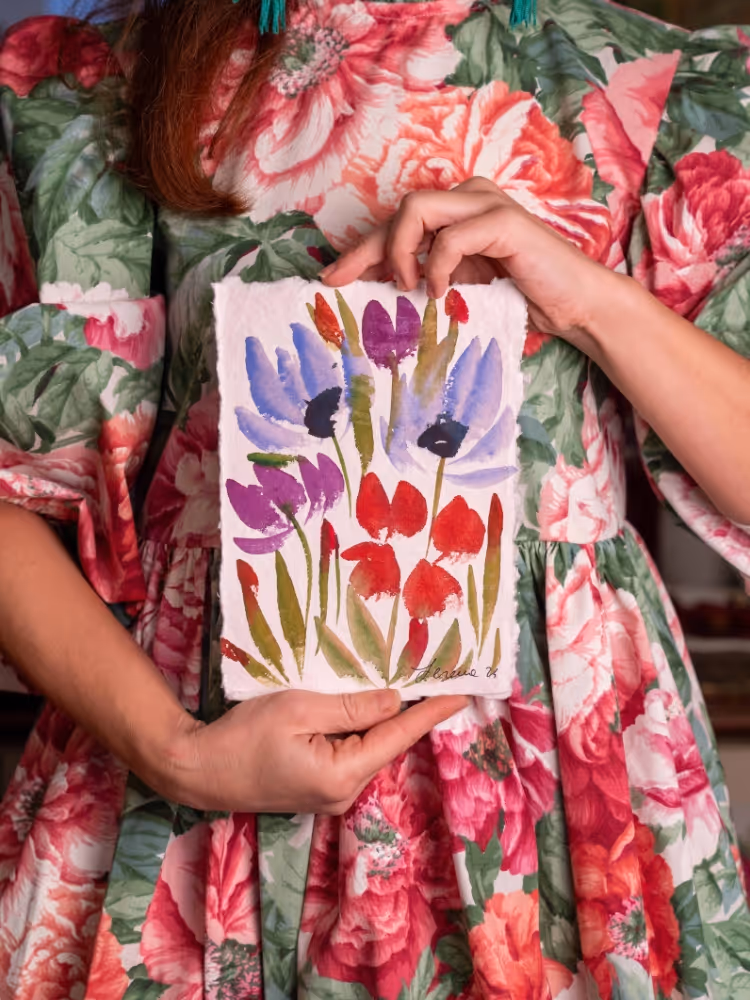 Serena holding a finished floral painting of purple and red tulips on handmade paper.