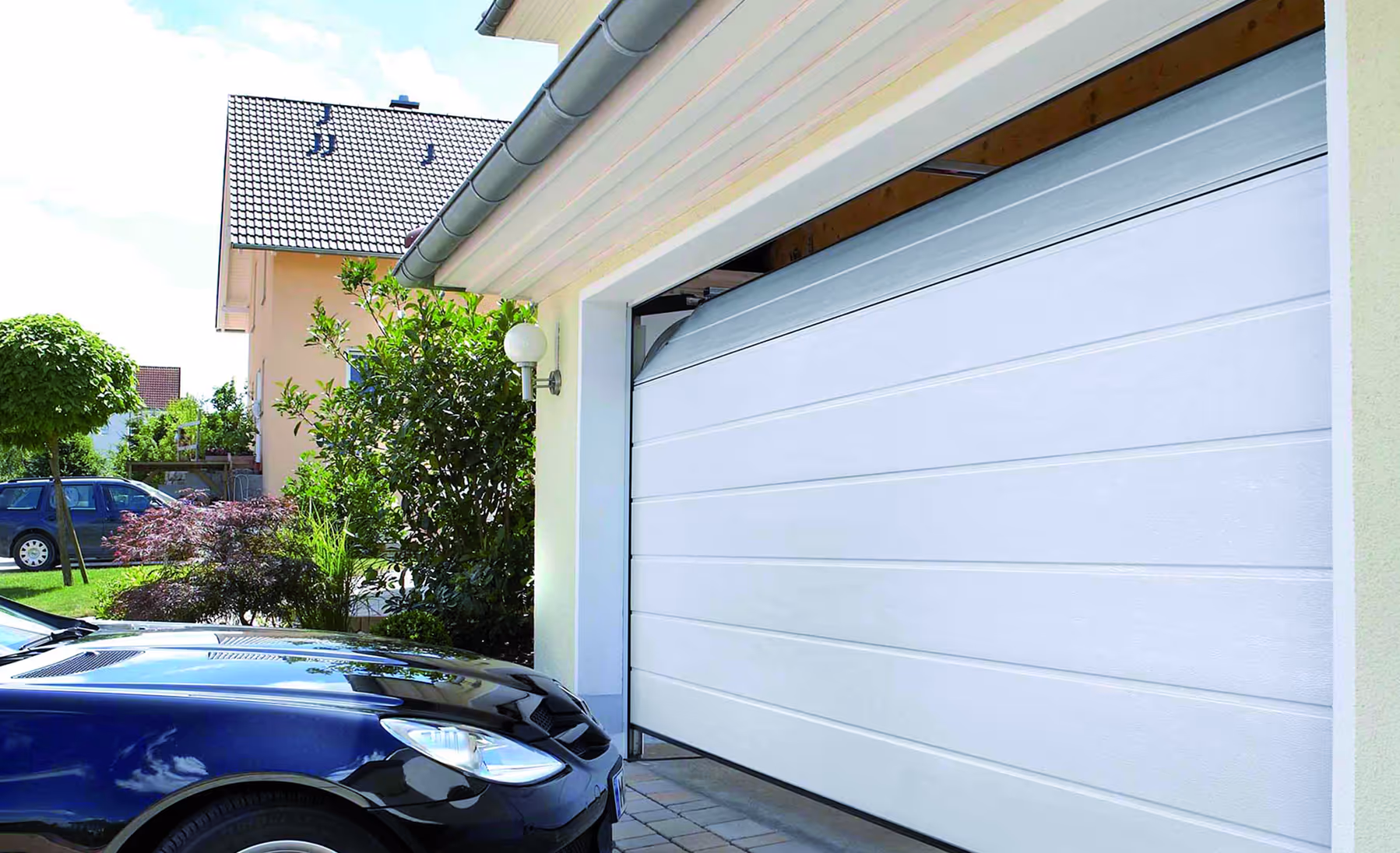 Weißes Garagentor, das sich öffnet, mit einem schwarzen Auto davor und einem Haus mit Garten im Hintergrund.