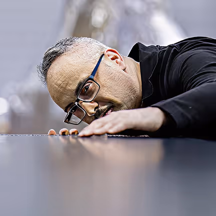 Ein Mann mit Brille und grauem Haar blickt konzentriert auf eine glatte Oberfläche.
