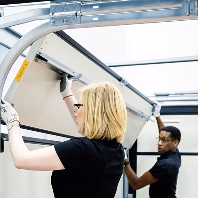 Zwei Personen, eine blonde Frau und ein Mann, montieren zusammen ein Garagentor.