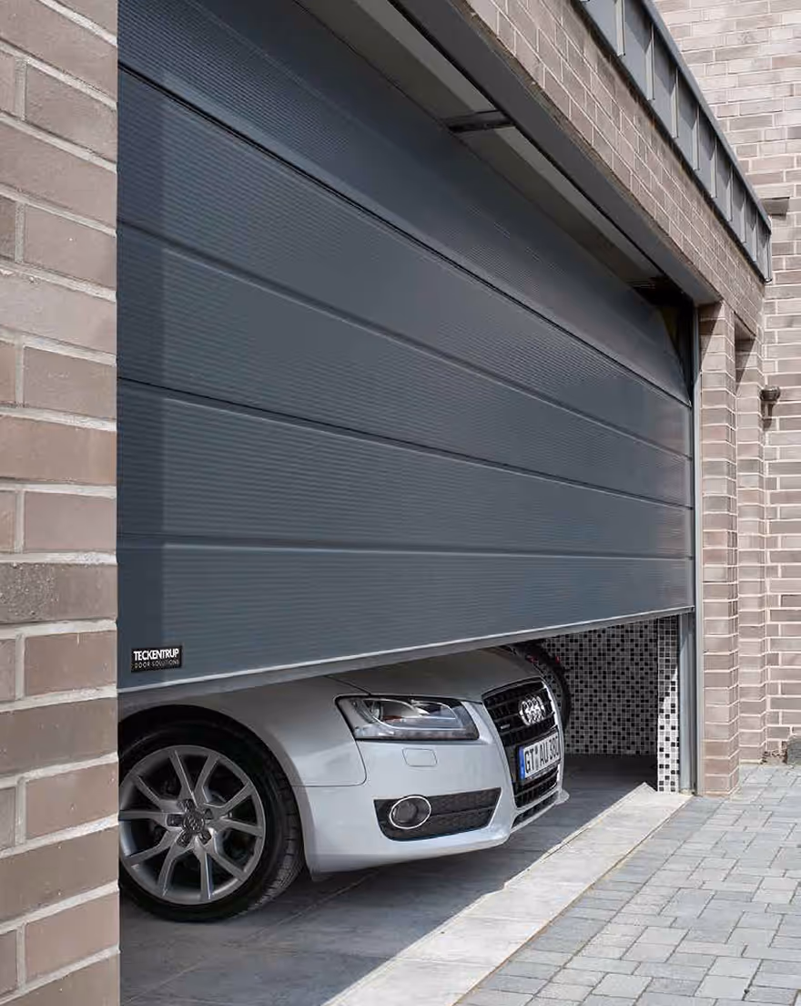 Teilweise geöffnete graue Garagentor mit teilweise sichtbarem silbernem Audi-Pkw davor.