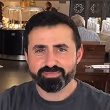 Porträt eines Mannes mit dunklem Haar und Bart in einem Restaurant.