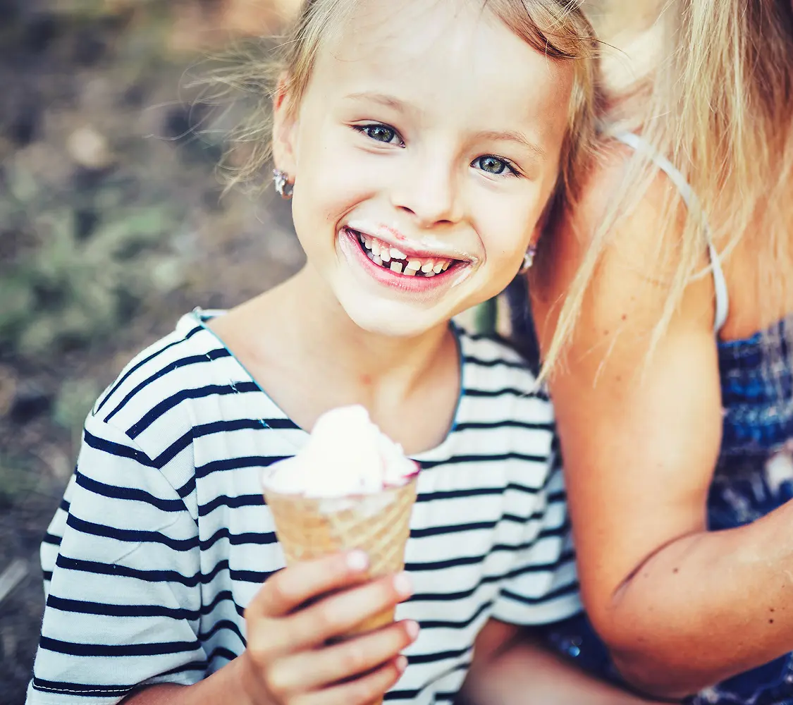 Smiling young child with a missing tooth holding an ice cream cone.