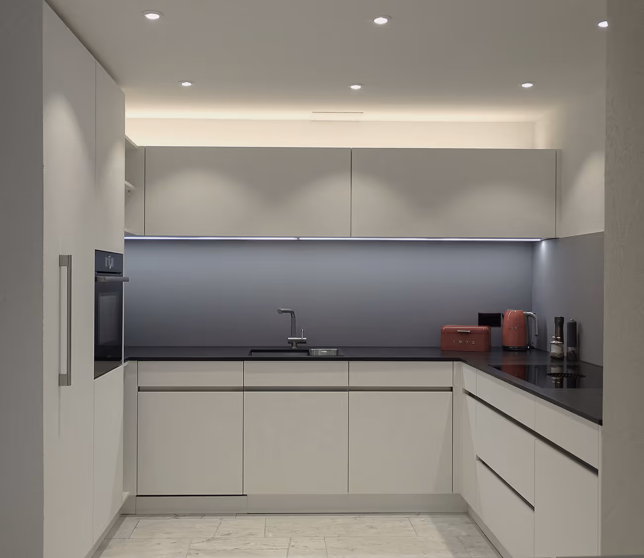 Moderne, minimalistische Küche mit grauen Schränken, schwarzen Arbeitsflächen, eingebautem Ofen, Spüle und roten Küchenkleingeräten.