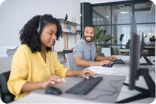 Smiling man and focused woman working at computers in a modern office.