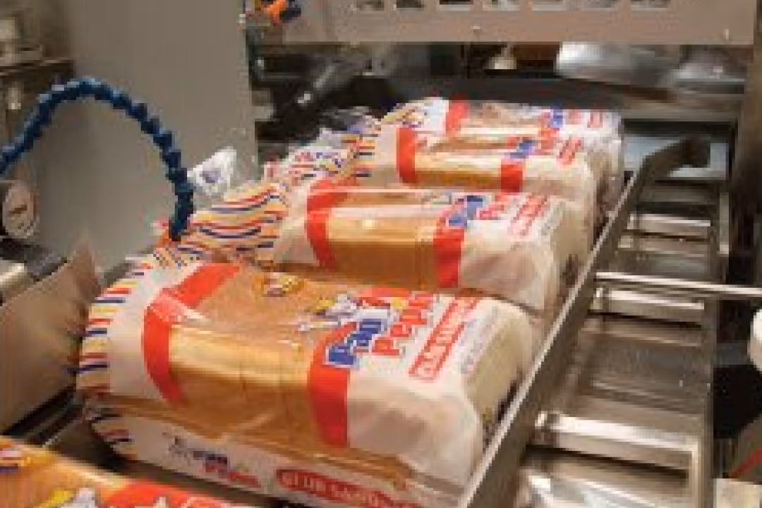 Slices of packaged bread lined up on a conveyor belt in a bakery or factory setting.