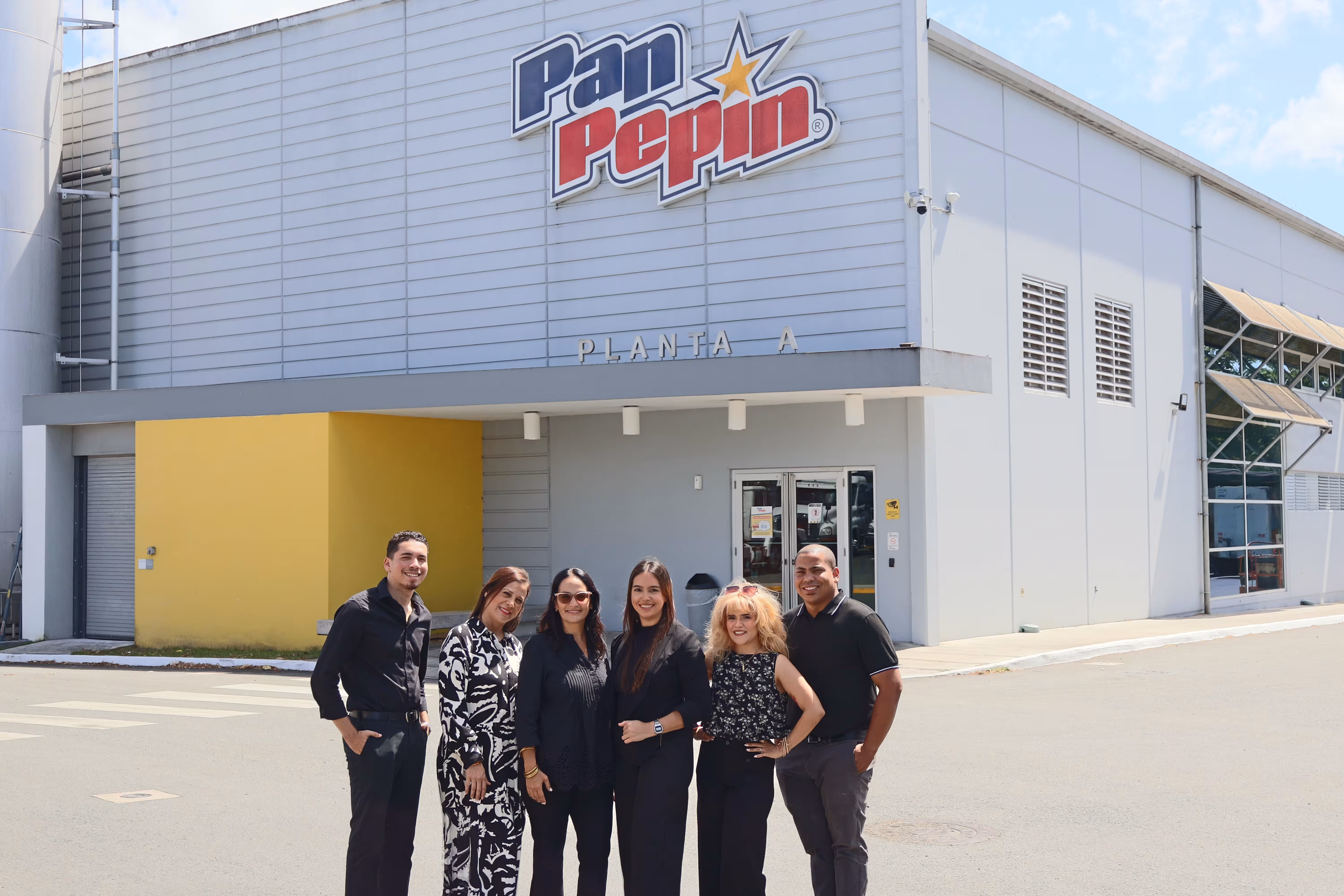 Six smiling employees standing outside a building with the Pan Pepin logo above the entrance labeled Planta A.
