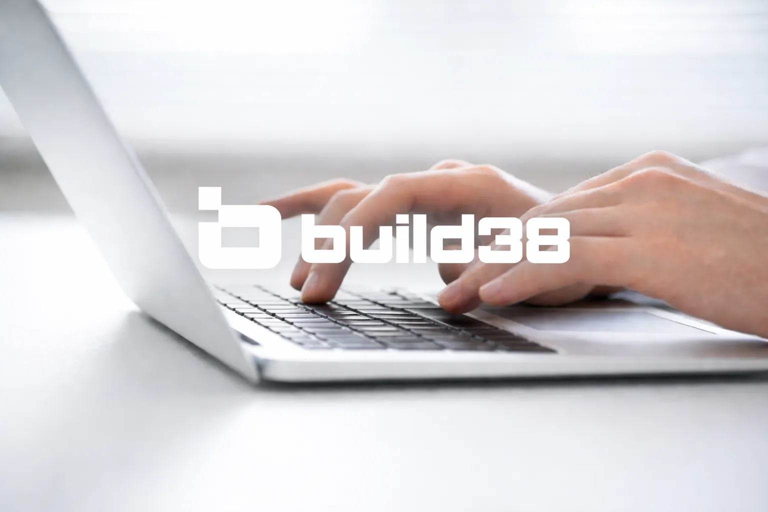 Hands typing on a laptop with the Build38 logo overlaid