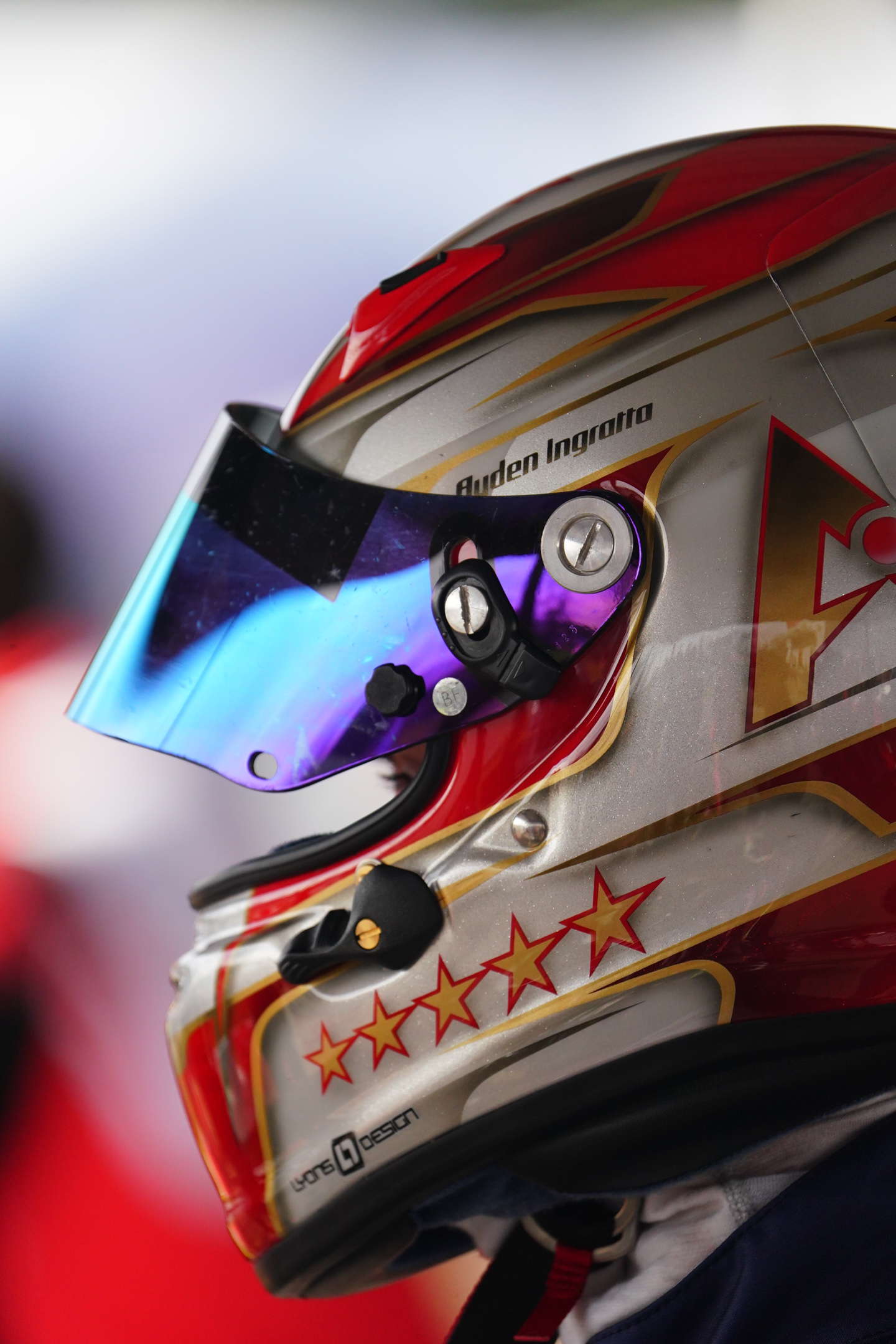 Close-up side view of a racing helmet with red and gold star designs and a reflective blue visor.