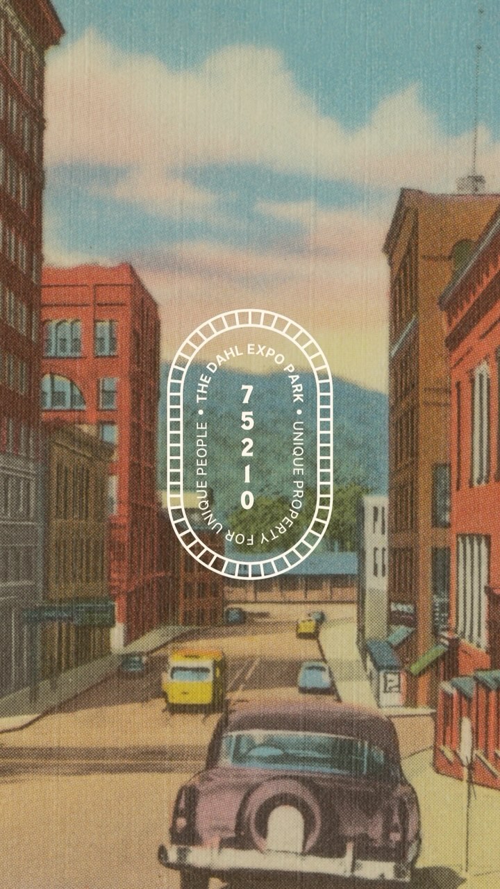 Vintage city street scene with classic cars and brick buildings under a blue sky.