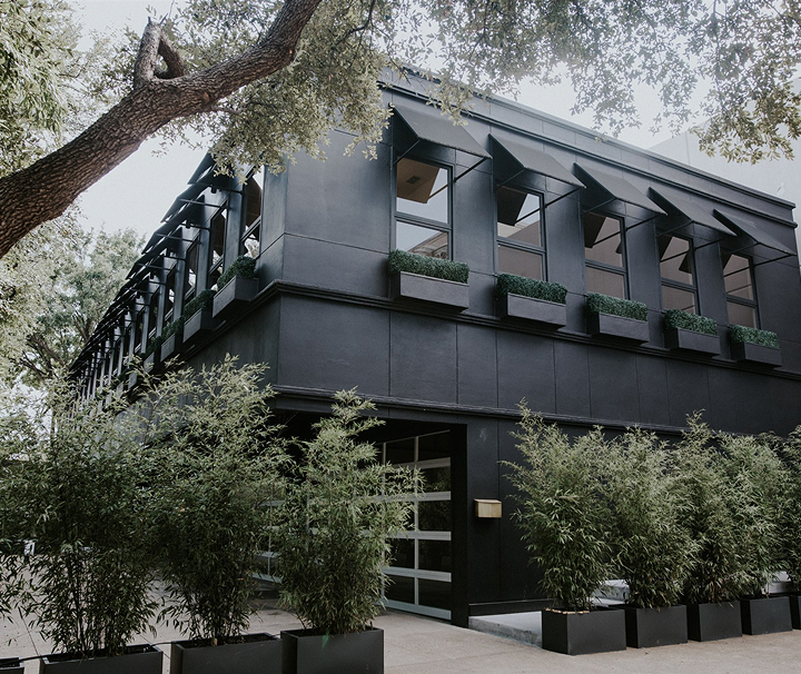Modern black two-story building with rectangular windows and greenery in planters outside.