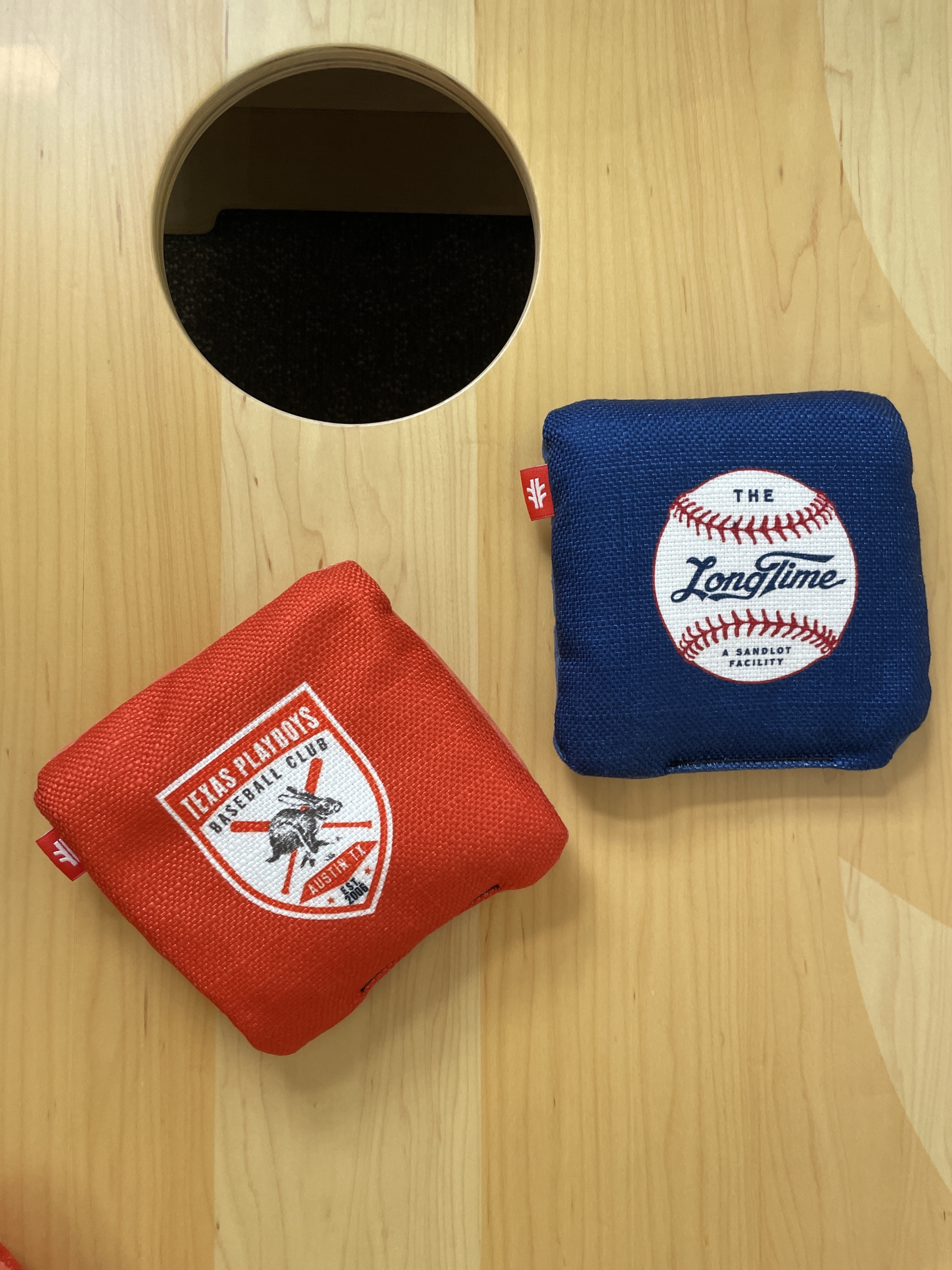 Red and blue cornhole bags on a wooden board near a circular hole.