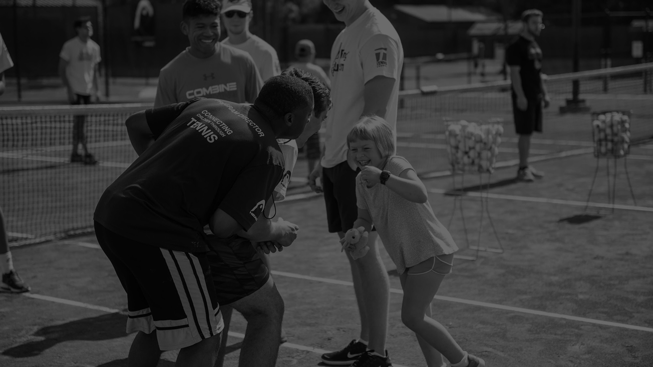 A young girl laughing with two men on a tennis court during a group tennis event.
