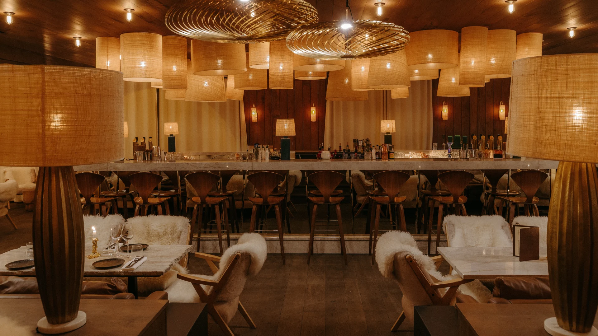 Panoramic view of the bar area at ChaCha restaurant in Megève, Annie Famose group (AFGroupe), with its central counter and rattan light fixtures.