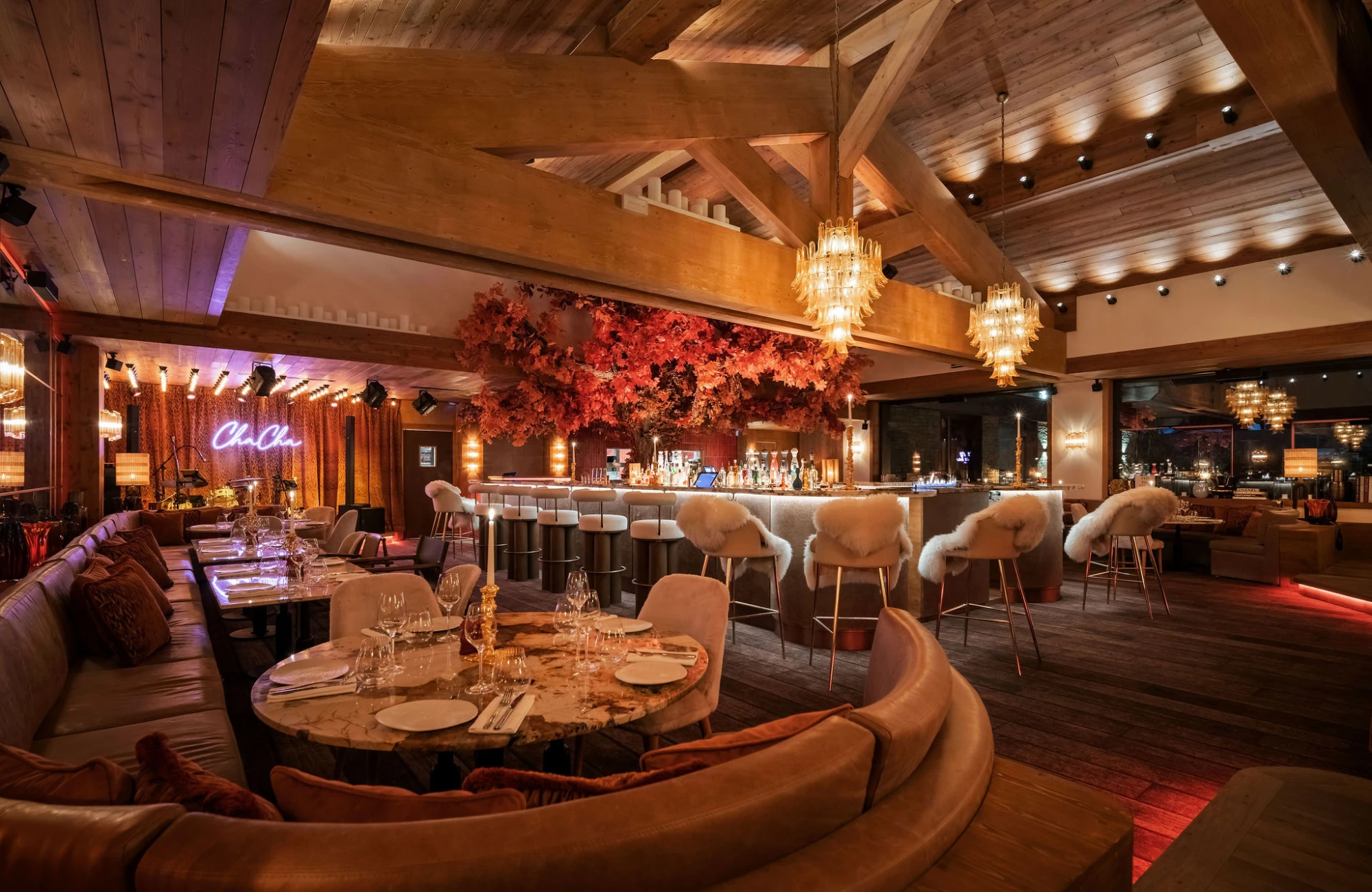 The plush interior of the ChaCha restaurant in Courchevel, part of the Annie Famose Group (AFGroupe), with its rounded banquettes, elegant tables, and majestic lighting fixtures.