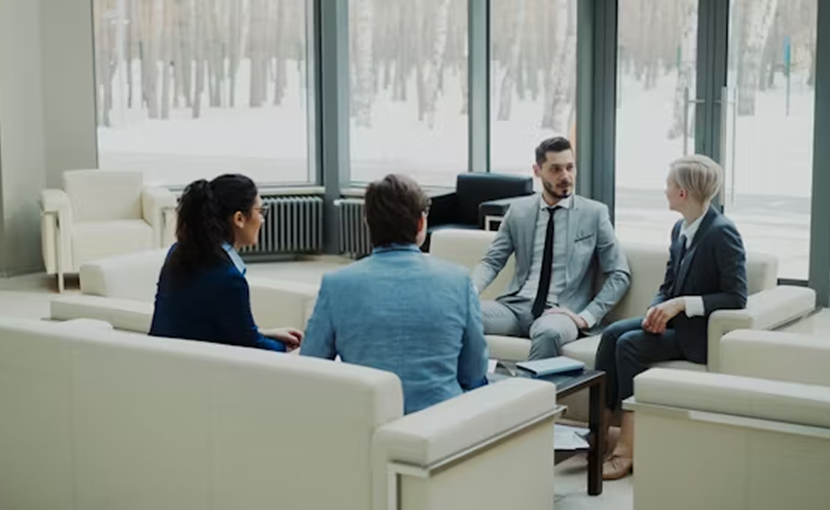 Four business professionals in suits sitting in a modern office lounge having a discussion.