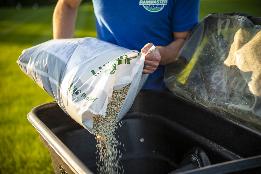 lawn team pours fertilizer into spreader