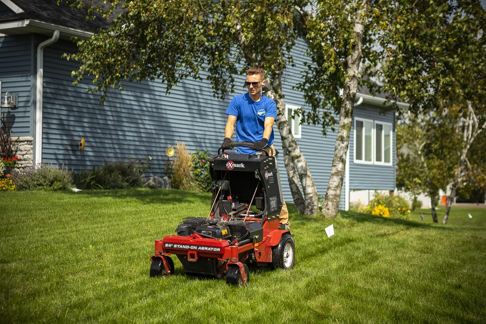 lawn care technician operating a powered lawn aerator