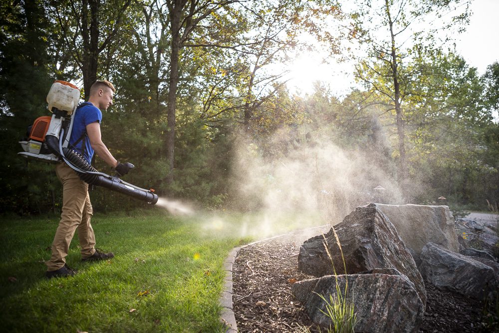 pest control technician applying mosquito barrier spray to a planting bed
