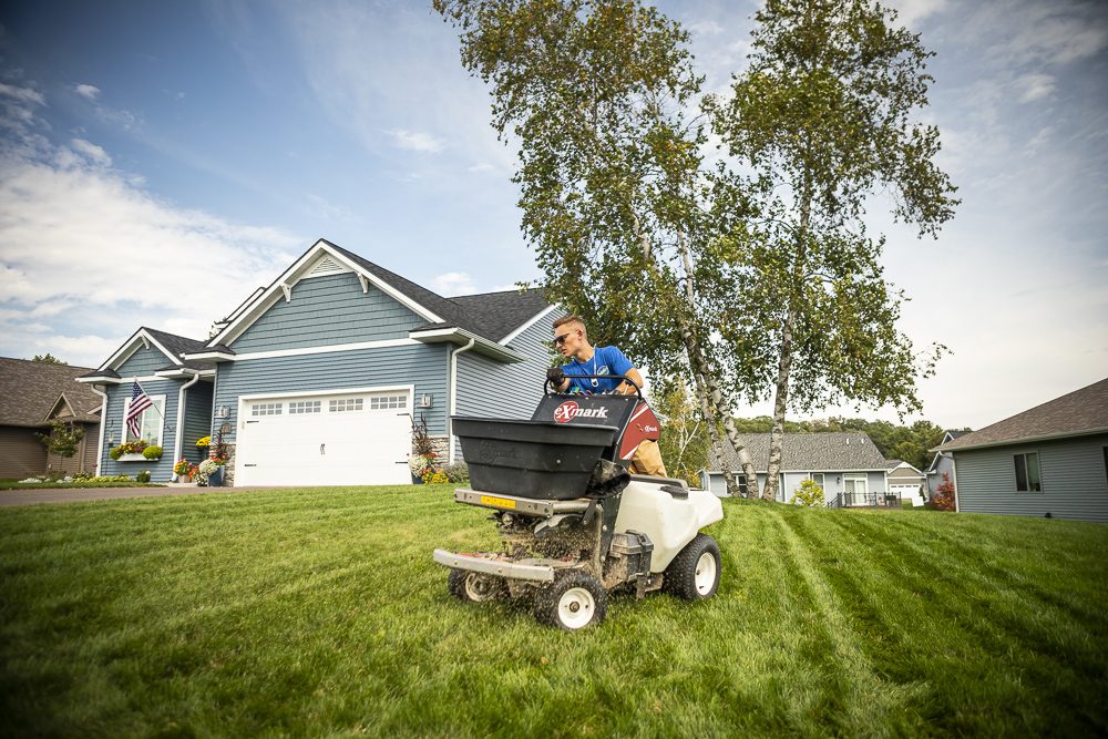 lawn care technician spreading granular fertilizer on a minnesota lawn