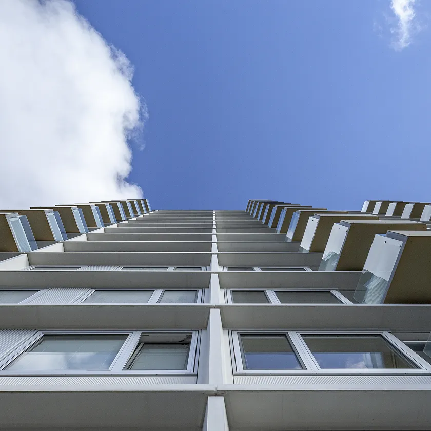 Blick von unten auf ein modernes hohes Wohngebäude mit Balkonen und blauem Himmel mit Wolken.
