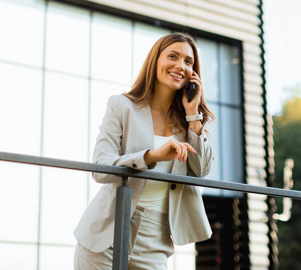 Ein lächelnder Handwerker mit blauer Arbeitskleidung und Ausweis hält einen roten Werkzeugkasten und spricht mit einer Frau in einem rosa T-Shirt im Hausflur.