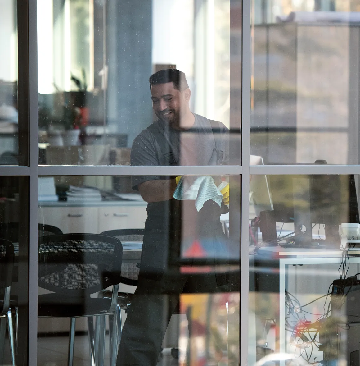 Mann in Arbeitskleidung, der ein Fenster in einem Bürogebäude putzt und dabei lächelt.