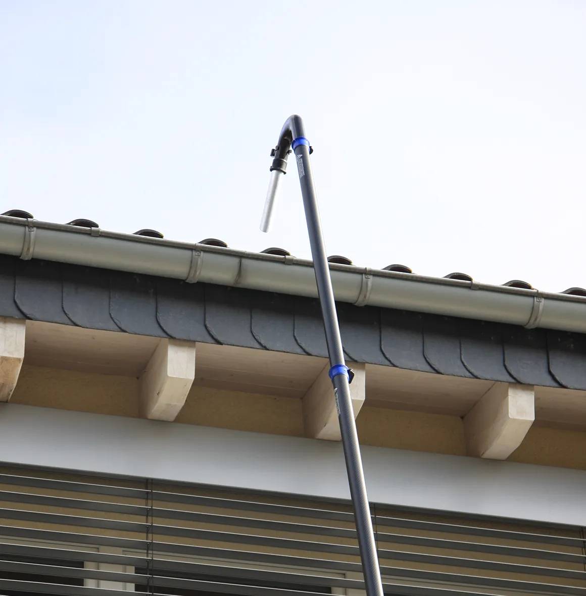 Ein langes Teleskoprohr mit einem gebogenen Ende steht vor einem Hausdach mit einer Regenrinne.