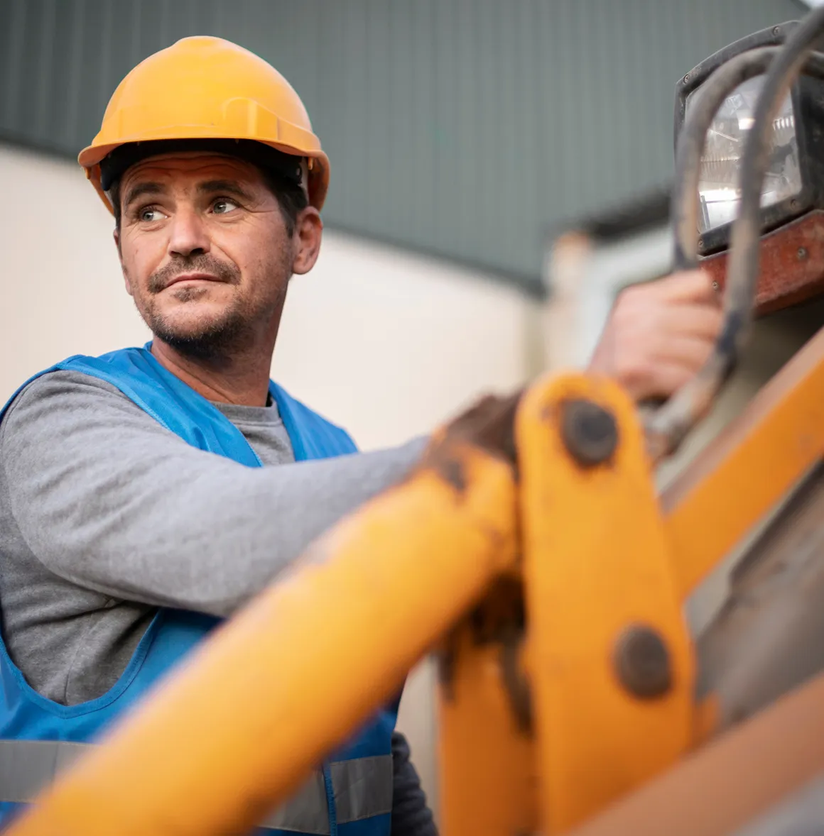 Bauarbeiter mit gelbem Helm und blauer Weste, der eine Baumaschine bedient.