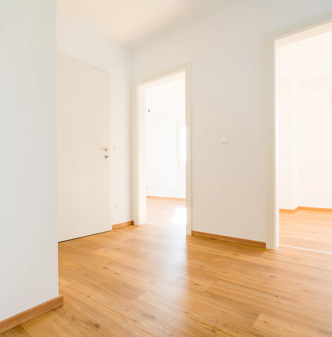 Heller Flur mit Holzboden und zwei offenen Türen zu hellen Räumen.