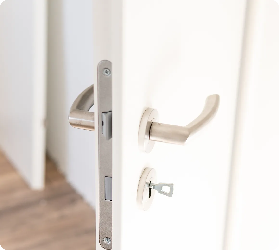 Nahaufnahme einer weißen Tür mit silbernem Türgriff und einem in das Schloss eingesteckten Schlüssel.