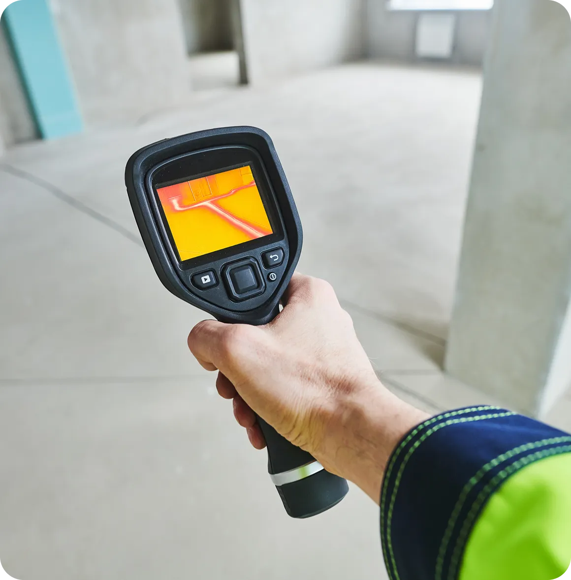 Hand hält Wärmebildkamera, die heiße Stellen auf dem Boden eines leeren Raums anzeigt.