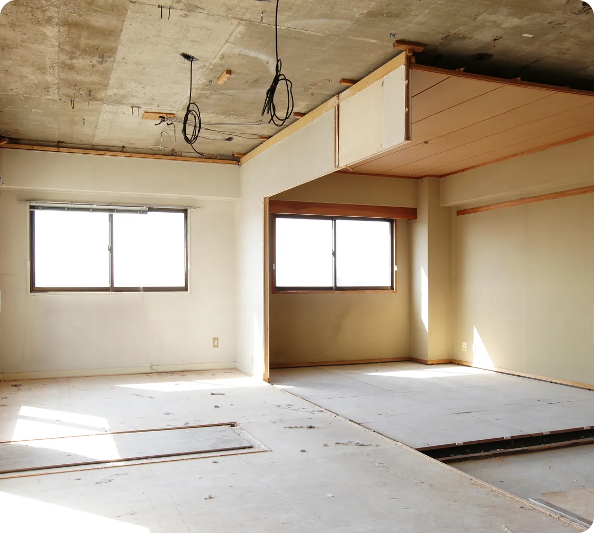 Leerer Raum mit zwei großen Fenstern, unvollständiger Decke und vorbereitetem Boden für Renovierung.