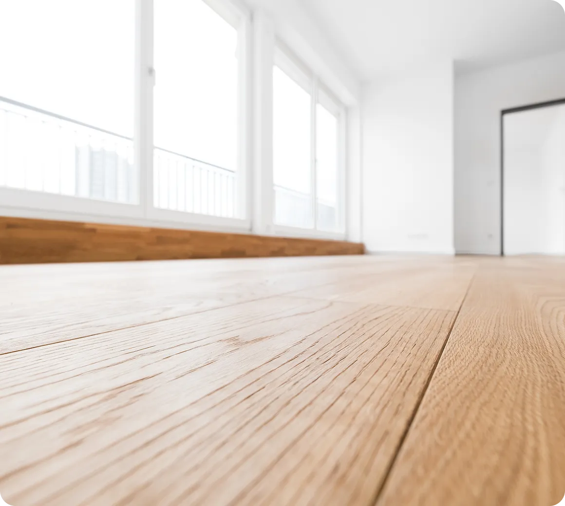 Nahaufnahme eines hellen Holzfußbodens in einem leeren, modernen Raum mit großen Fenstern.