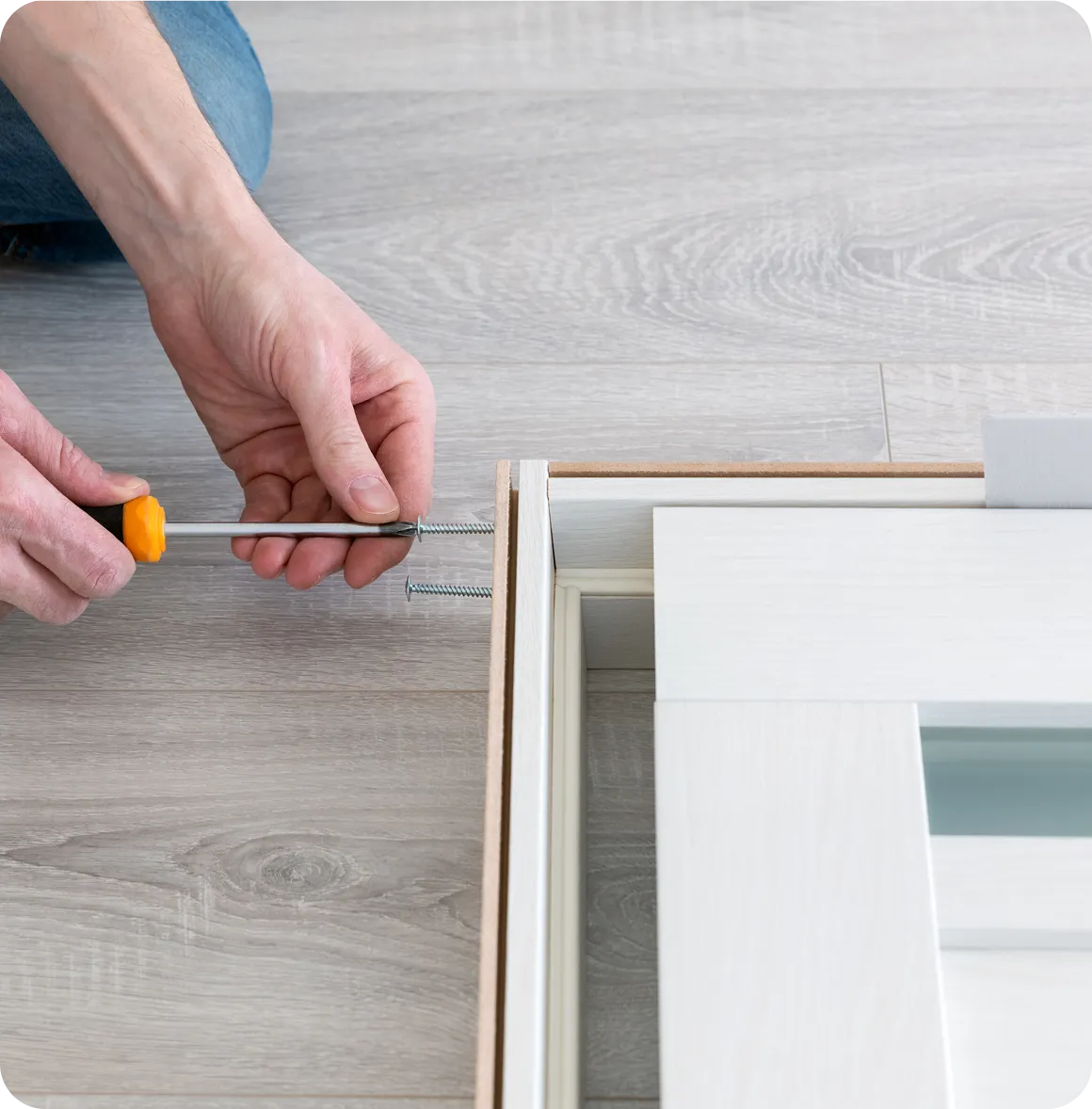 Eine Person verwendet einen Schraubendreher, um Schrauben in einen weißen Türrahmen auf einem hellgrauen Holzboden zu drehen.