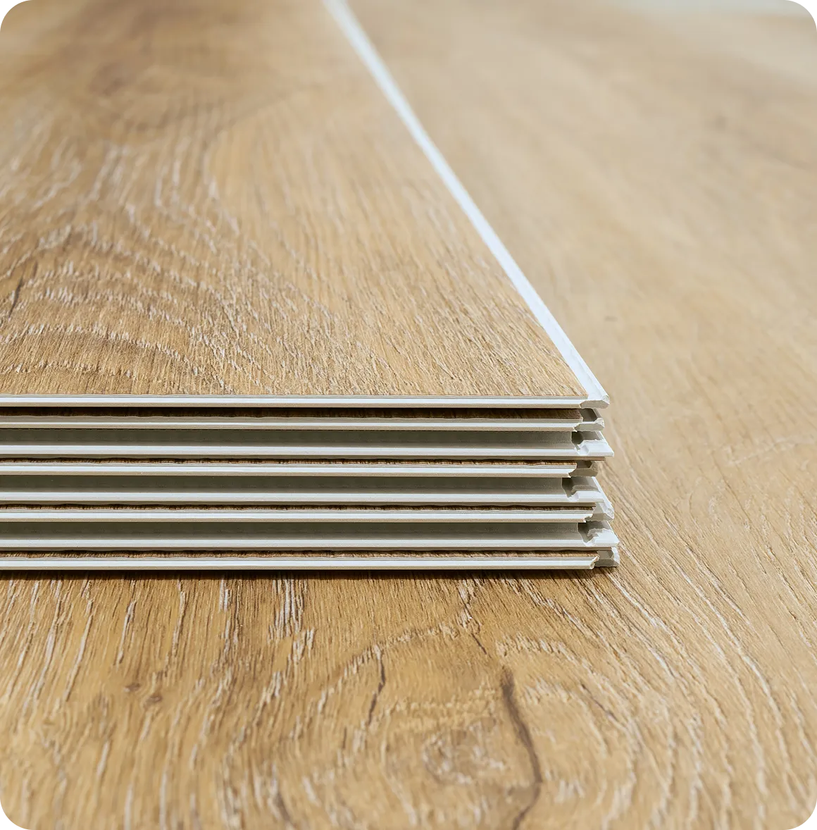 Aufgeschichtete Laminatbretter mit Holzmaserung auf hellem Holzboden.